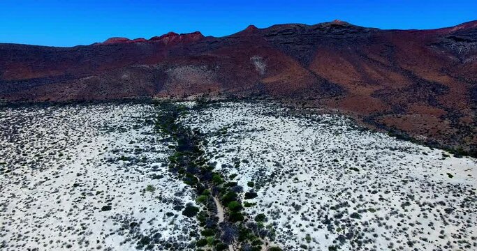 Ascending Forward Aerial Over Barren Desert to Reddish Brown Mountainous Backdrop
