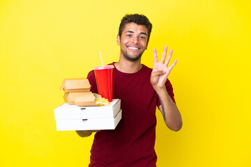 Young brazilian man holding pizzas and burgers isolated background happy and counting four with fingers