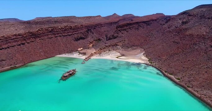 Backward Flying Aerial of Desert Beach Cove with Unique Volcanic Mountains, Bright Turquoise Water and Anchored Sailboats
