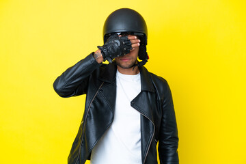 Young Brazilian man with a motorcycle helmet isolated on yellow background covering eyes by hands....