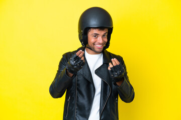 Young Brazilian man with a motorcycle helmet isolated on yellow background making money gesture