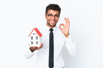 Fototapeta na wymiar Young business Brazilian man holding a house toy isolated on white background showing ok sign with fingers