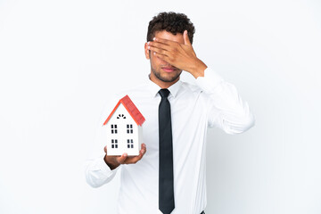 Young business Brazilian man holding a house toy isolated on white background covering eyes by hands. Do not want to see something