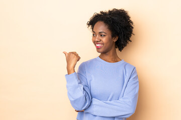 Young African American woman isolated on beige background pointing to the side to present a product