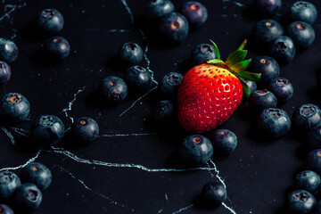 Overhead shot of  fresh blueberries with a strawberry in the middle on dark background. 