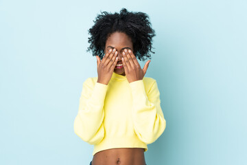 Young African American woman isolated on blue background covering eyes by hands