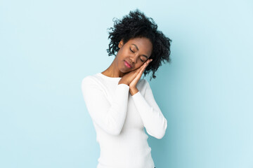 Young African American woman isolated on blue background making sleep gesture in dorable expression