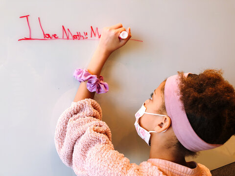 Young girl wearing a mask writing on a whiteboard