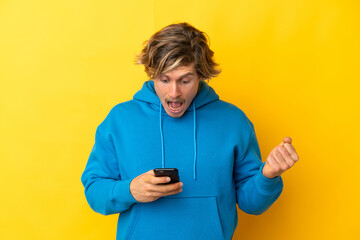 Handsome blonde man isolated on yellow background surprised and sending a message