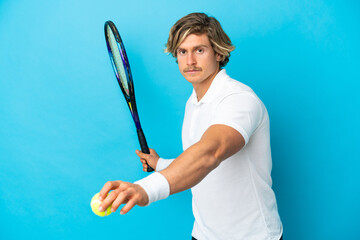 Young blonde man isolated on blue background playing tennis