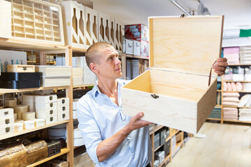 Adult European man choosing wooden trunk in housewares store.