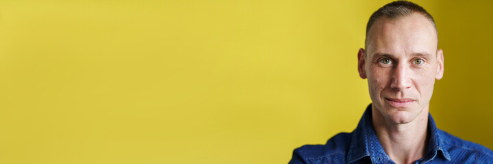 Front view close up portrait of male adult caucasian man with short blonde hair and green eyes in front of yellow background looking to the camera smiling with copy space