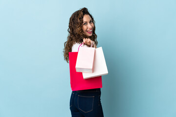 Young caucasian woman isolated on blue background holding shopping bags and smiling