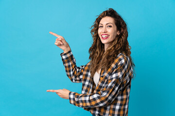 Young caucasian woman isolated on blue background pointing finger to the side and presenting a product