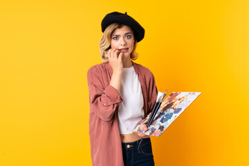 Young artist girl holding a palette isolated on yellow background nervous and scared