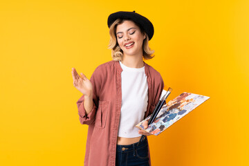 Young artist girl holding a palette isolated on yellow background laughing