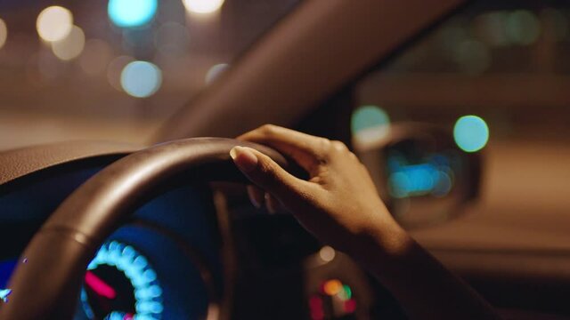 woman driving car with hands on steering wheel in city at night travelling on the road to destination 