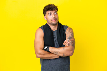 Young sport caucasian man with towel isolated on yellow background making doubts gesture while...