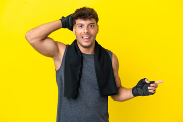 Young sport caucasian man with towel isolated on yellow background surprised and pointing finger to the side