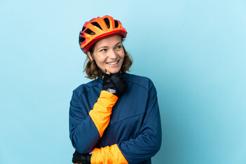Young cyclist woman isolated on blue background looking up while smiling