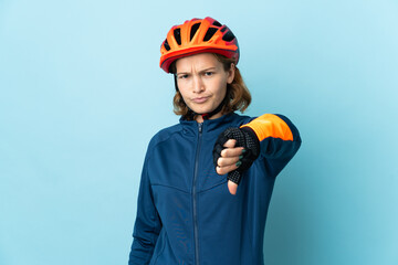 Young cyclist woman isolated on blue background showing thumb down with negative expression