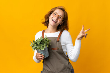 Young Georgian woman holding a plant isolated on yellow background smiling and showing victory sign