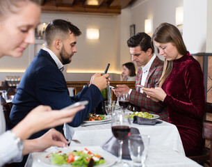 Modern young people busying with phone during evening meal at restaurant