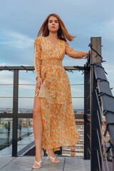 A girl in long dress standing on the stairs on the top of the roof of building.
