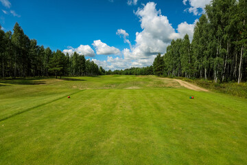 Fototapeta na wymiar Golf course, landscape, green grass on the background of the forest and a bright sky with clouds. High quality photo