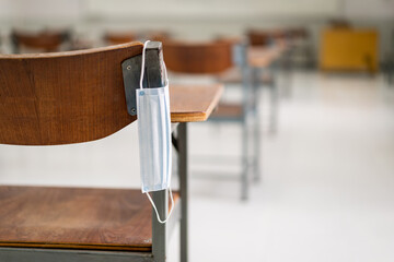 Education during COVID-19: A used medical facemask hangs on a wood lecture chair in empty classroom during COVID-19 pandemic