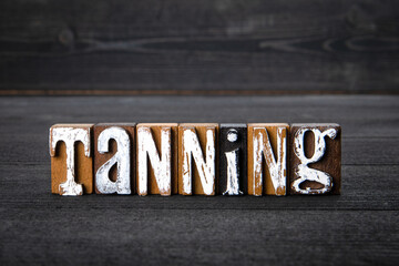 Tanning. White wooden letters on a dark wooden background
