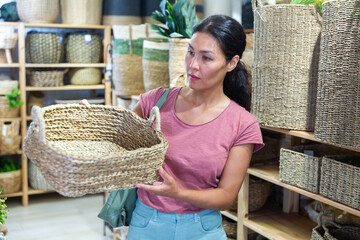 Asian woman standing and choosing wicker basket in housewares store.