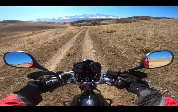 Riding motorcycle on off-road in mountains. Steering wheel view