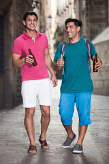 Two guys friends are walking and drinking beer in Barcelona