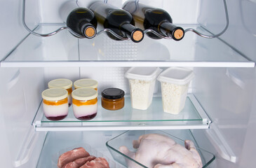 Obraz na płótnie Canvas on the shelf of the refrigerator are food, three bottles of wine, dairy bio-products, meat, chicken and steaks