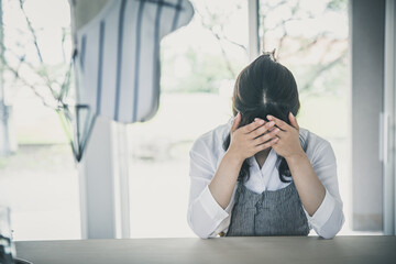 女性が窓のある部屋で座って頭を抱えている　woman window 