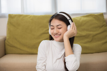 Relaxing time on sofa. Beautiful young asian woman lay down on sofa and listening to the music with headphone. She has rhythm Lifestyle in living room at house in the morning.