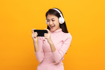 Beautiful young asian women play mobile game and put on wireless headphone standing on isolated...