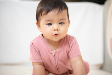 An Asian girl about 1 year old. Playing in the living room in the house. A cute baby wearing a pink dress Stay with parents in the house