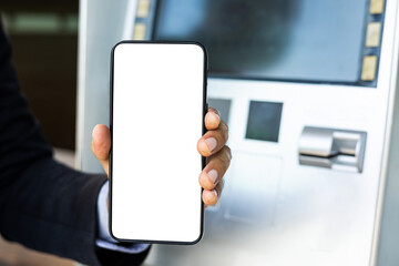 Young businessman standing front of atm machine using smartphone withdraw the money without atm credit card. He ut the pin code into smartphone and take the money.