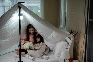 mom and little daughter play together on the couch hidden under a white blanket.