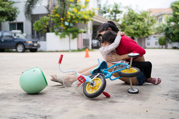 Mother comforting her daughter after she fell while riding her scooter