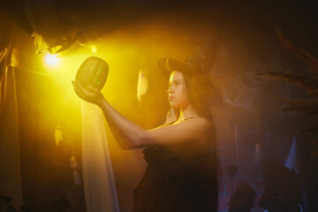 Young girl looking like witch having fun on Halloween in a dark room with yellow light and smoke. Teenager in Carnival and Halloween party