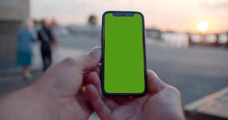 Pov bokeh shot of man hands holding modern black mobile phone with blank green screen.