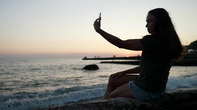 Happy time with a selfie on the beach silhouette. A slender woman with a smartphone takes photos of her mobile phone on the sea beach sunset for relaxation on a trip nature