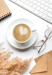 Office desk workspace with notebook, coffee and pampas grass.