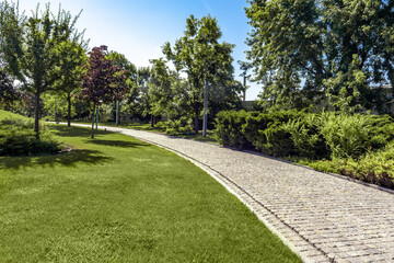 Fototapeta na wymiar Green parkland with neatly mowed lawn and paved path on summer day