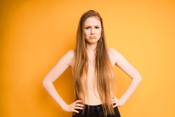 Caucasian girl with long hair, offended and put her hands on her belt, isolated on a yellow background