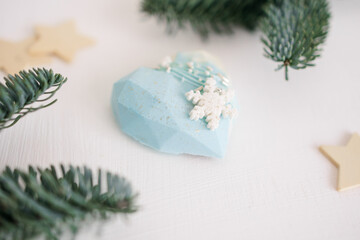 A heart-shaped cake covered with blue icing on a white background. Decor of spruce branches, decoration in the form of sugar snowflakes. Christmas and New Year.