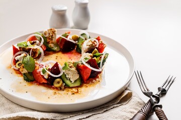 Appetizing and fresh vegetable salad with beetroot, goat cheese, ripe tomato, cucumber, mustard leaves and spicy sauce. Delicious and healthy lunch. Serving restaurant dish. Light background